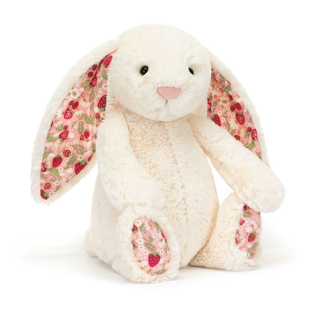 A cream-colored plush bunny toy with soft cotton ears and feet, featuring a pattern of strawberries and cream flowers on a pink backdrop.