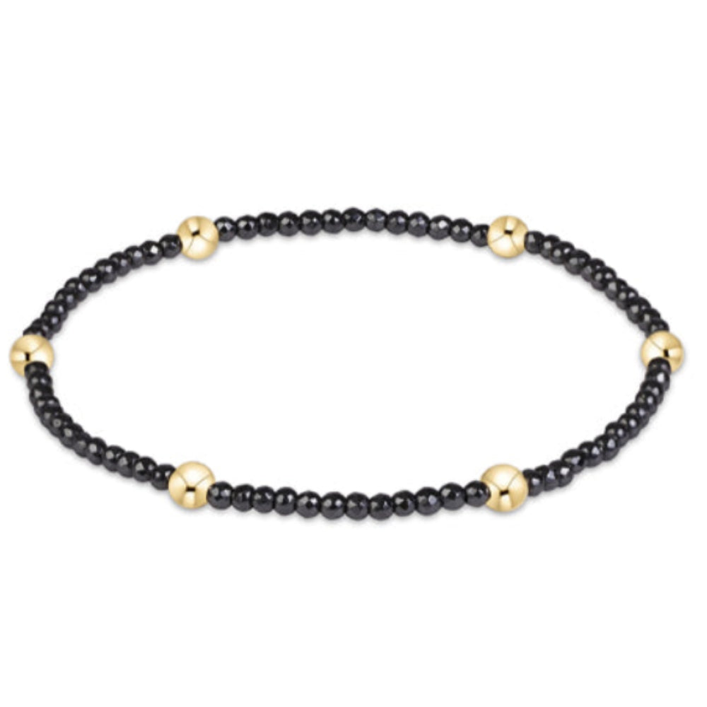 A delicate beaded bracelet featuring small black beads separated by tiny gold spacer beads, displayed on a clean white background.