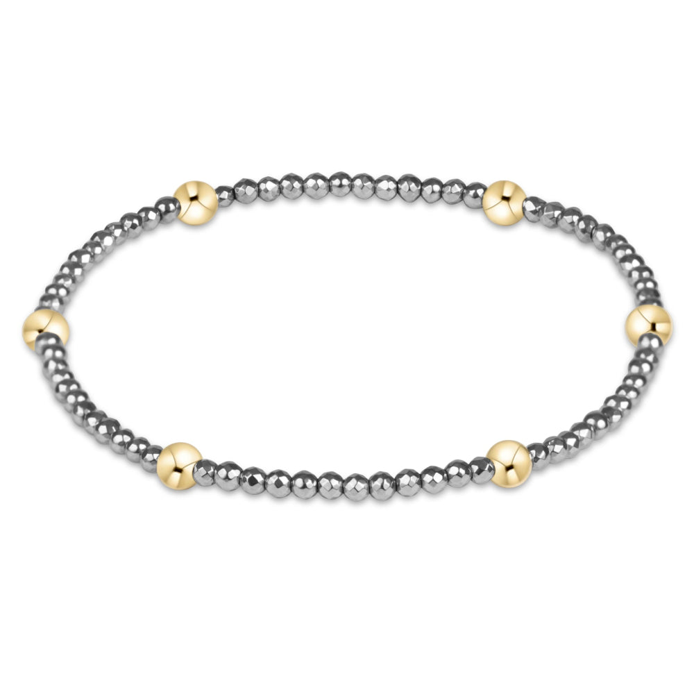 A delicate beaded bracelet featuring alternating rows of small dark gray beads and polished gold-toned round beads, displayed on a clean white background.