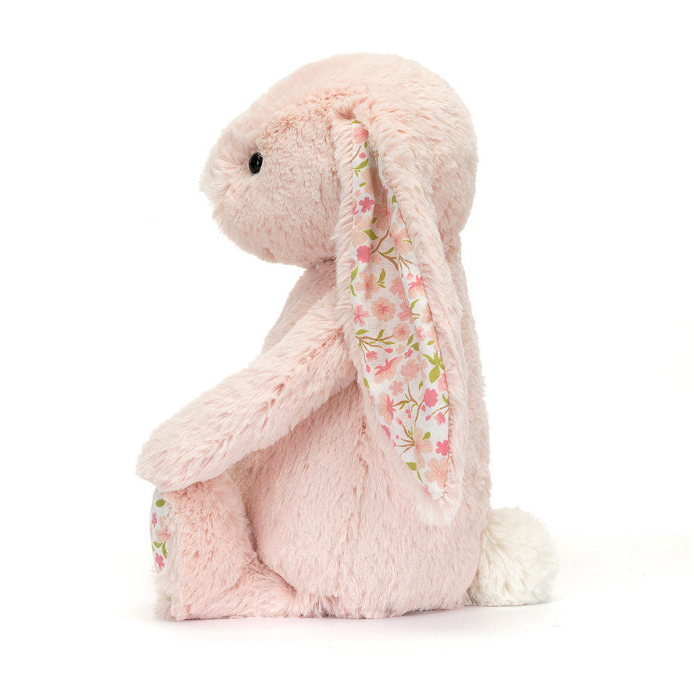 A side photo of a medium/original sized pink plush bunny with  floral-patterned ears on a white background.