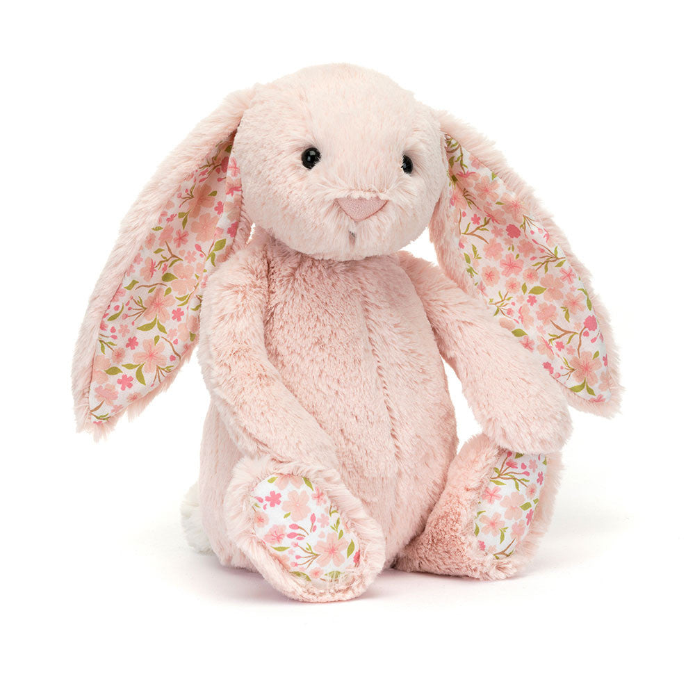 A side angled photo of a medium/original sized pink plush bunny with  floral-patterned ears on a white background.
