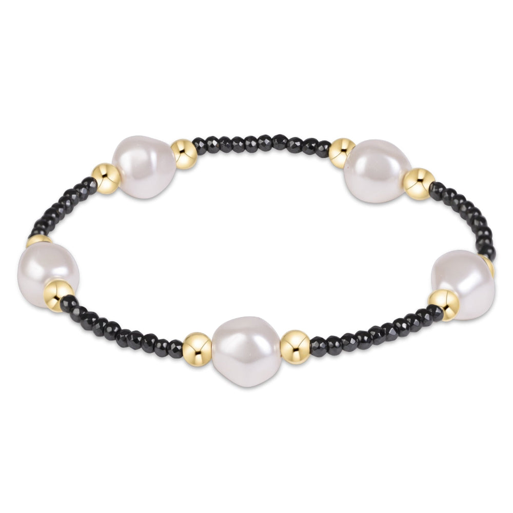 A beaded stretch bracelet featuring large white freshwater pearls, small black seed beads, and polished gold spacer beads, displayed on a clean white background.