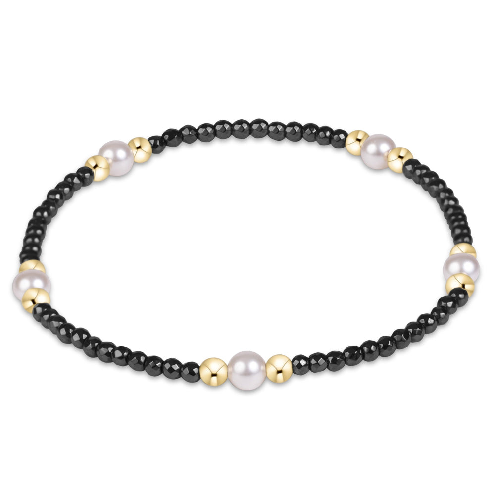 A beaded stretch bracelet featuring small black beads, larger white pearls, and small gold spacer beads, displayed on a clean white background.