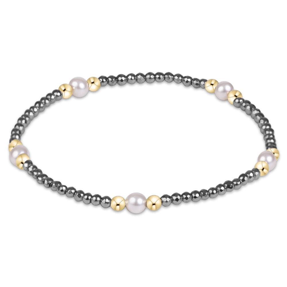 A delicate beaded bracelet featuring dark gray metallic beads, small gold spacer beads, and a few white pearl-like accents, displayed on a clean white background.
