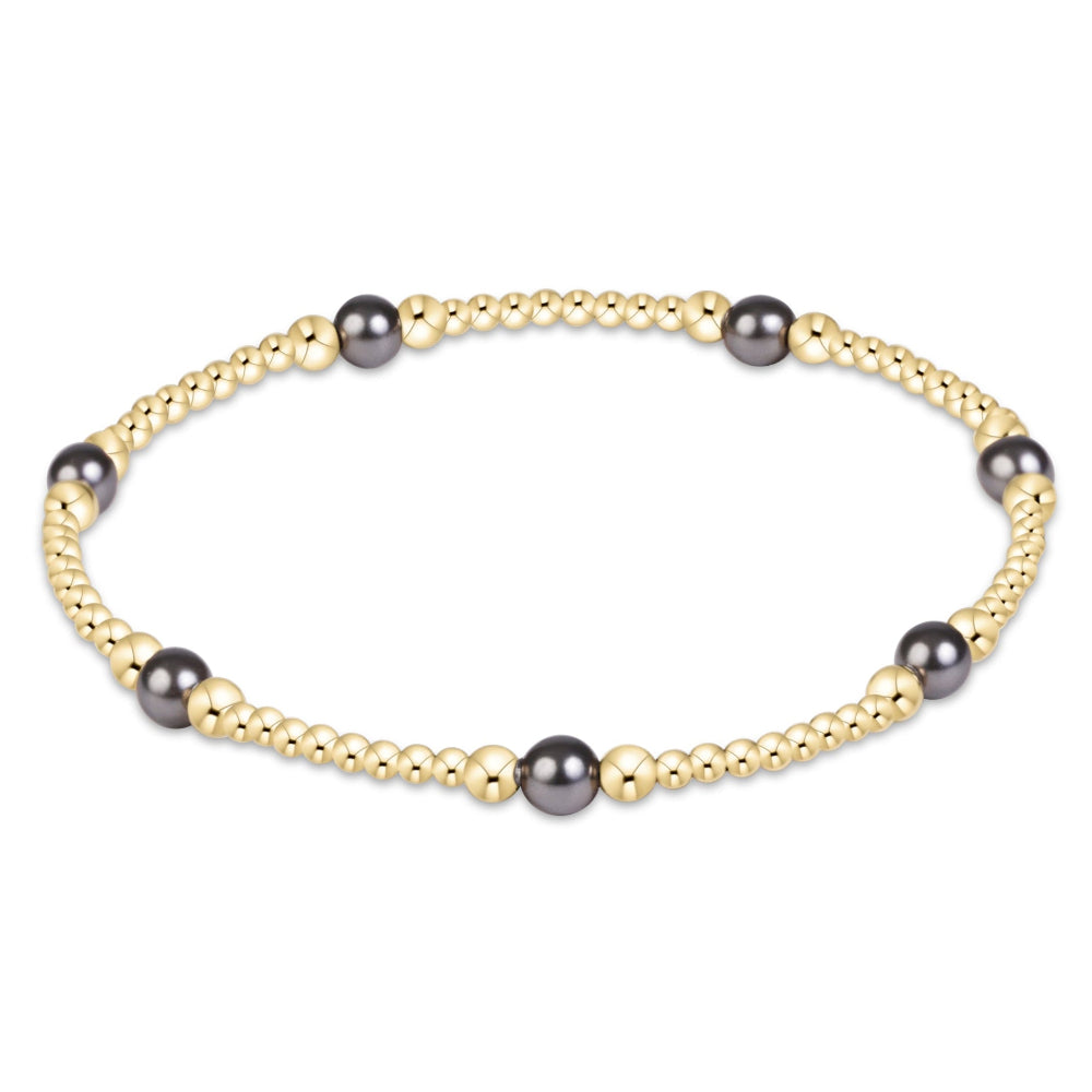 A delicate gold beaded bracelet with alternating dark gray round pearls and small gold spacer beads, displayed on a clean white background.
