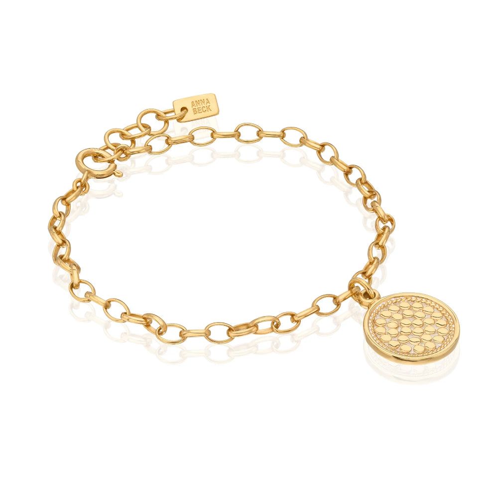A gold chain bracelet with a textured circular disc charm, displayed on a clean white background with a soft reflection.