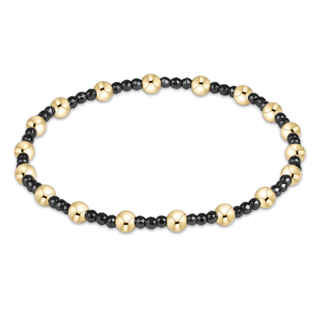 A beaded stretch bracelet featuring alternating polished gold-tone round beads and smaller matte black round beads, displayed on a clean white background.