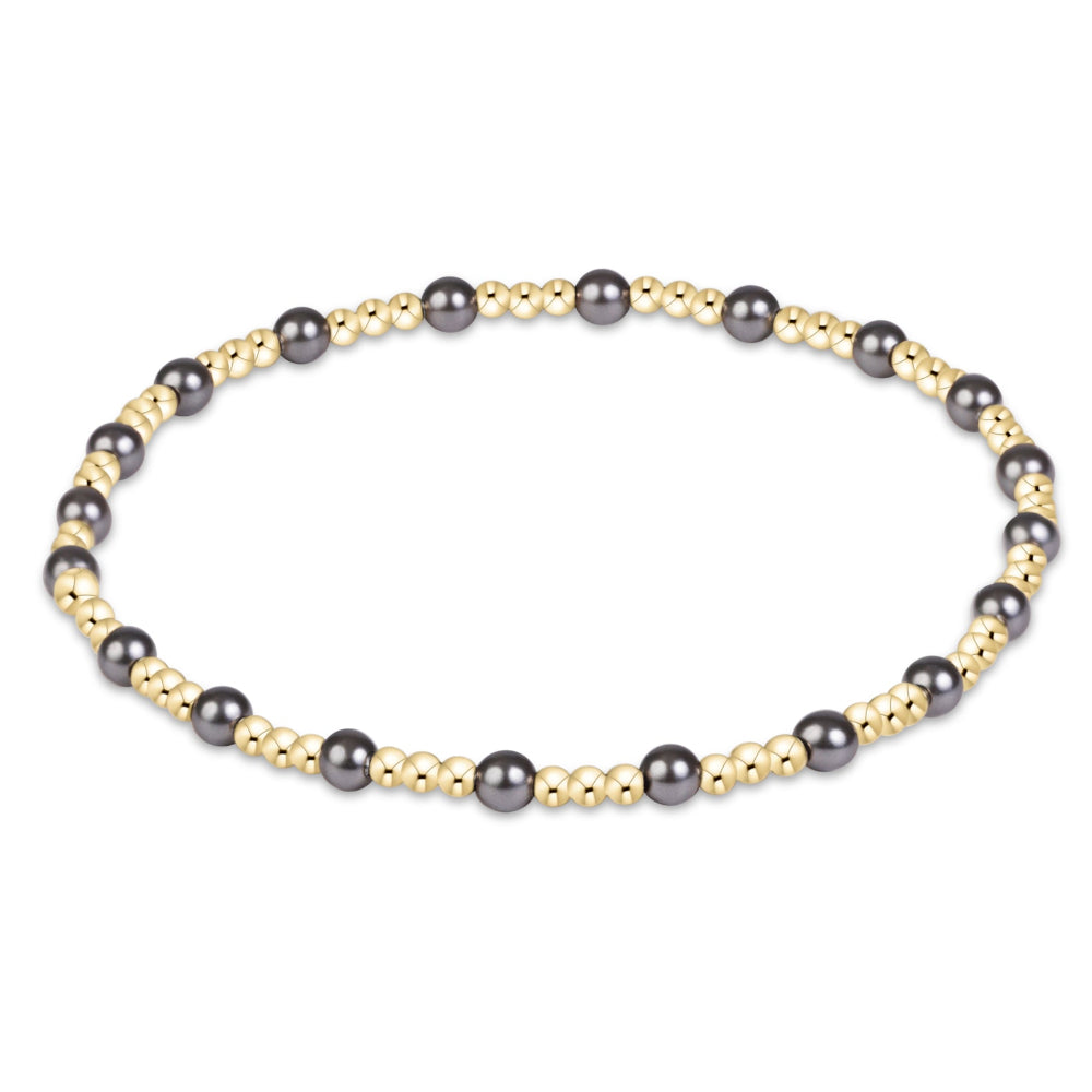 A beaded stretch bracelet featuring alternating dark gray/black round beads and small metallic gold spacer beads, displayed on a clean white background.
