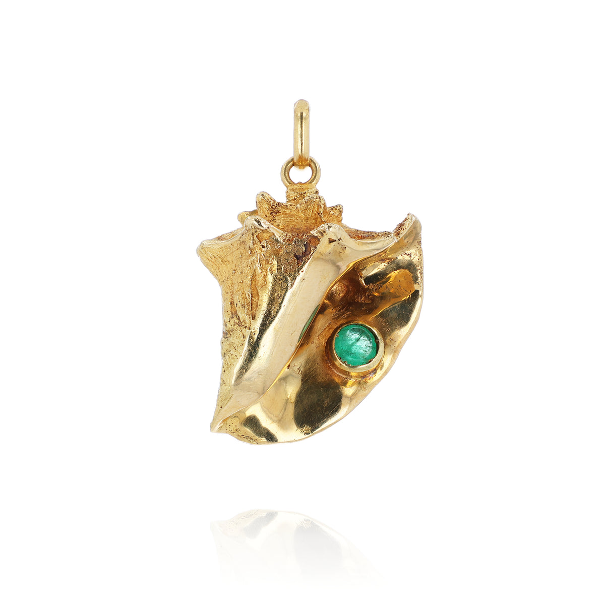 A gold conch shell pendant featuring a small round emerald inset, shown on a clean white background with a soft reflection below.