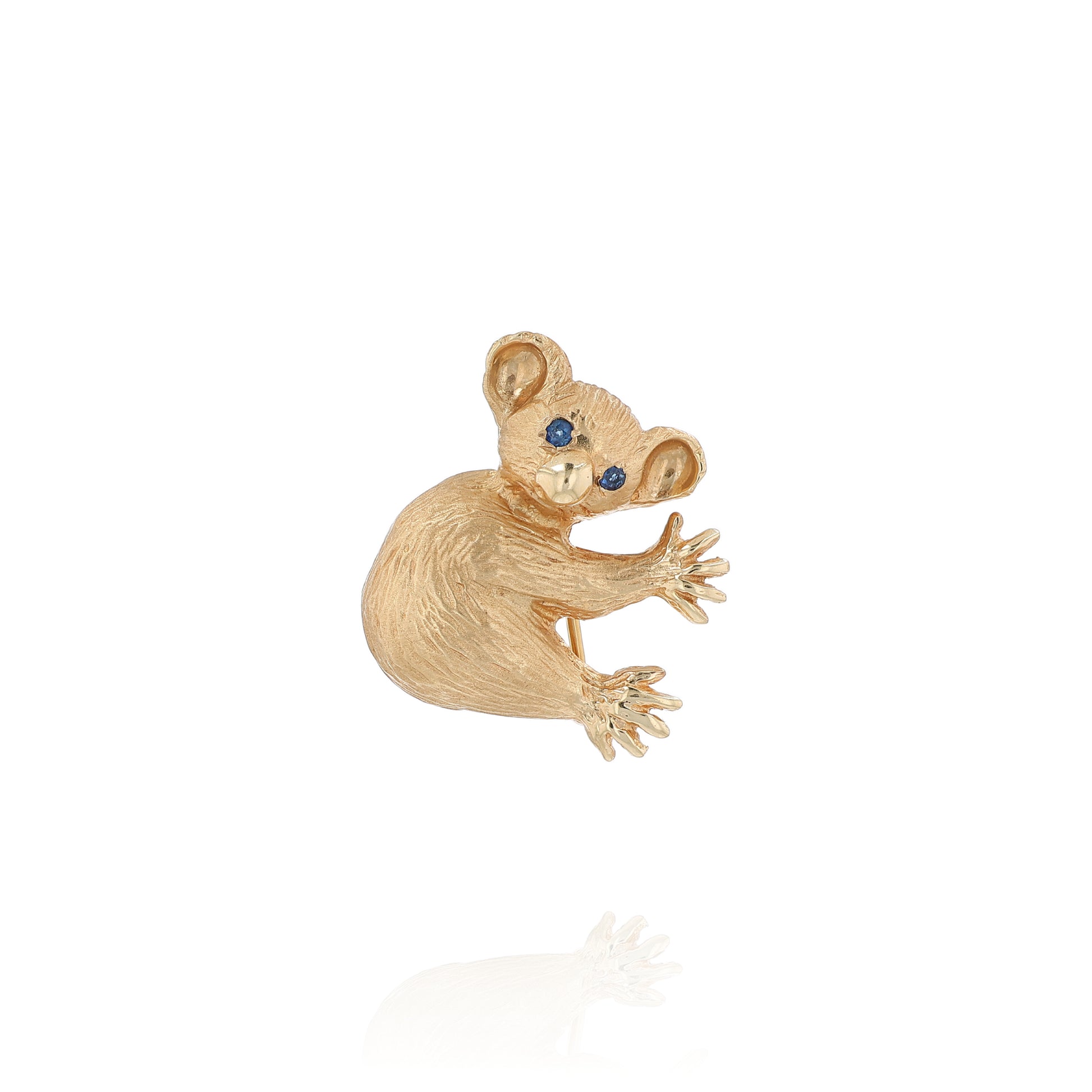 Yellow gold brushed koala pin with two round blue sapphire eyes on a white background