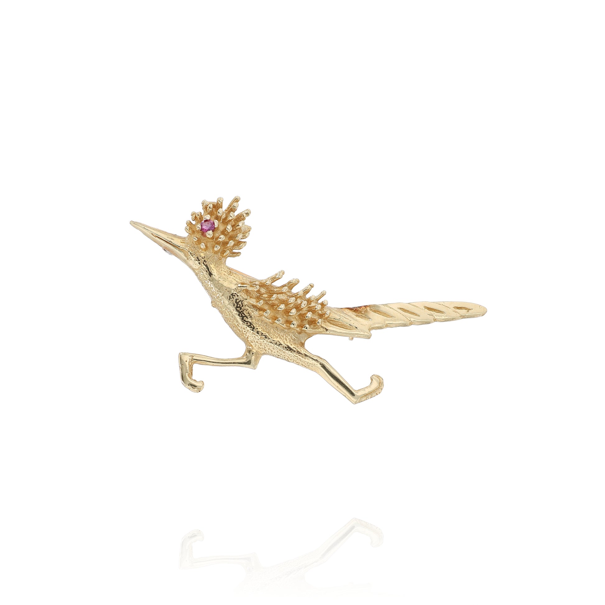 Yellow gold road runner pin with a round pink sapphire eye on a white background
