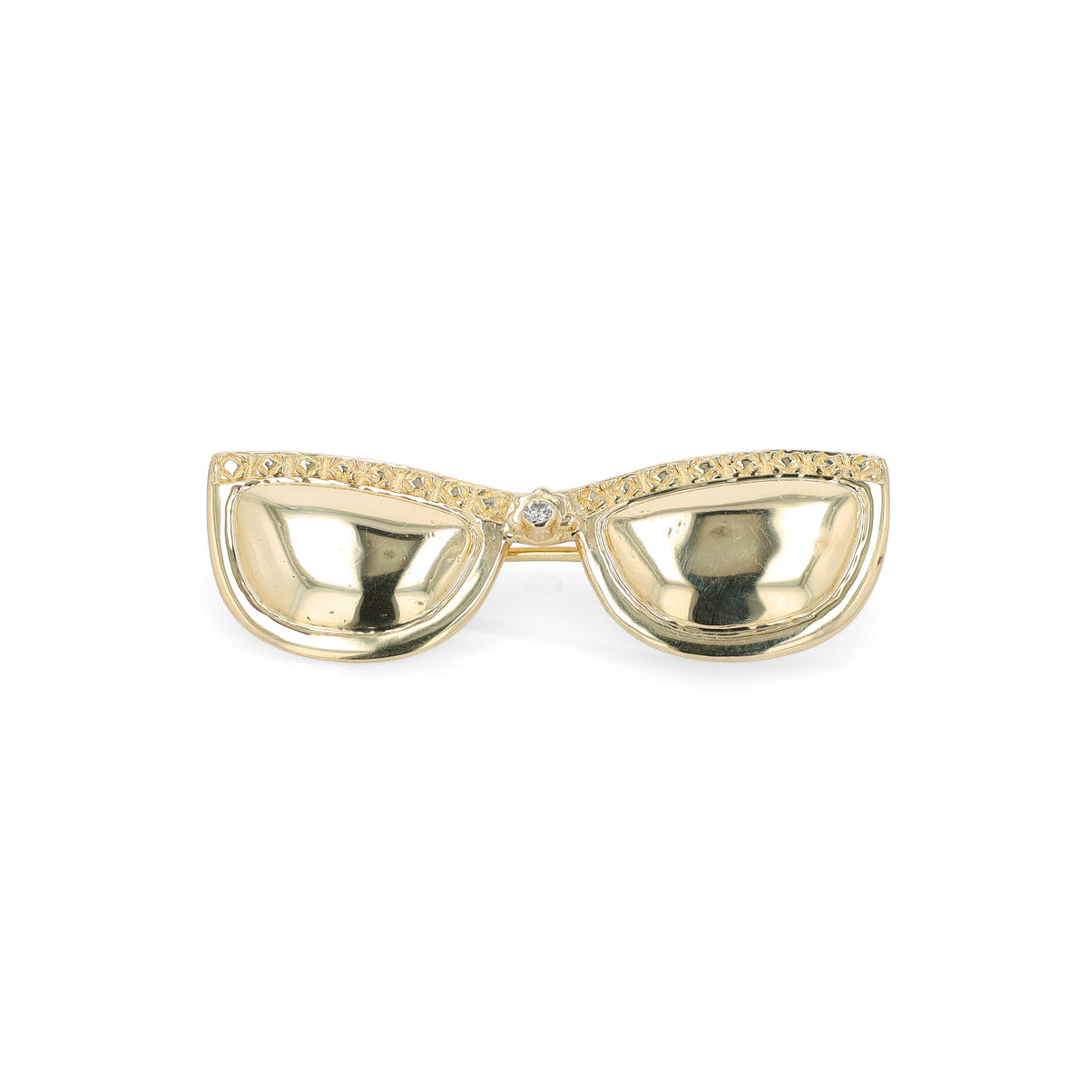A gold brooch depicting sunglasses with a row of textured gold along the top frame and a central diamond, shown on a plain white background.