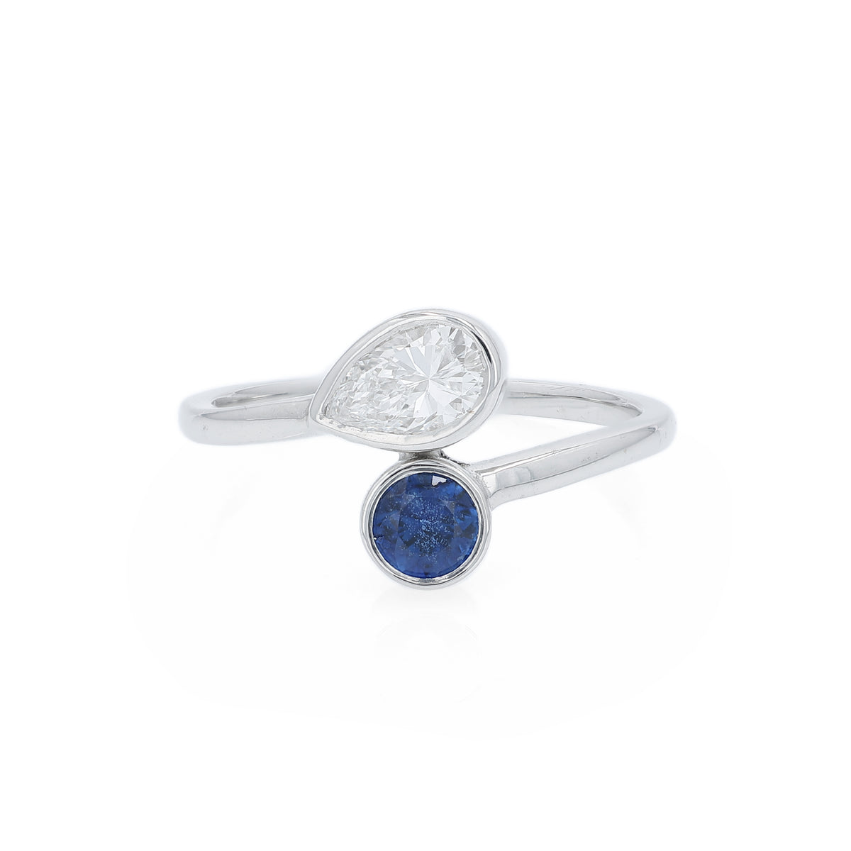 A white gold ring featuring a pear-cut diamond and a round-cut deep blue sapphire, set on a clean white background.
