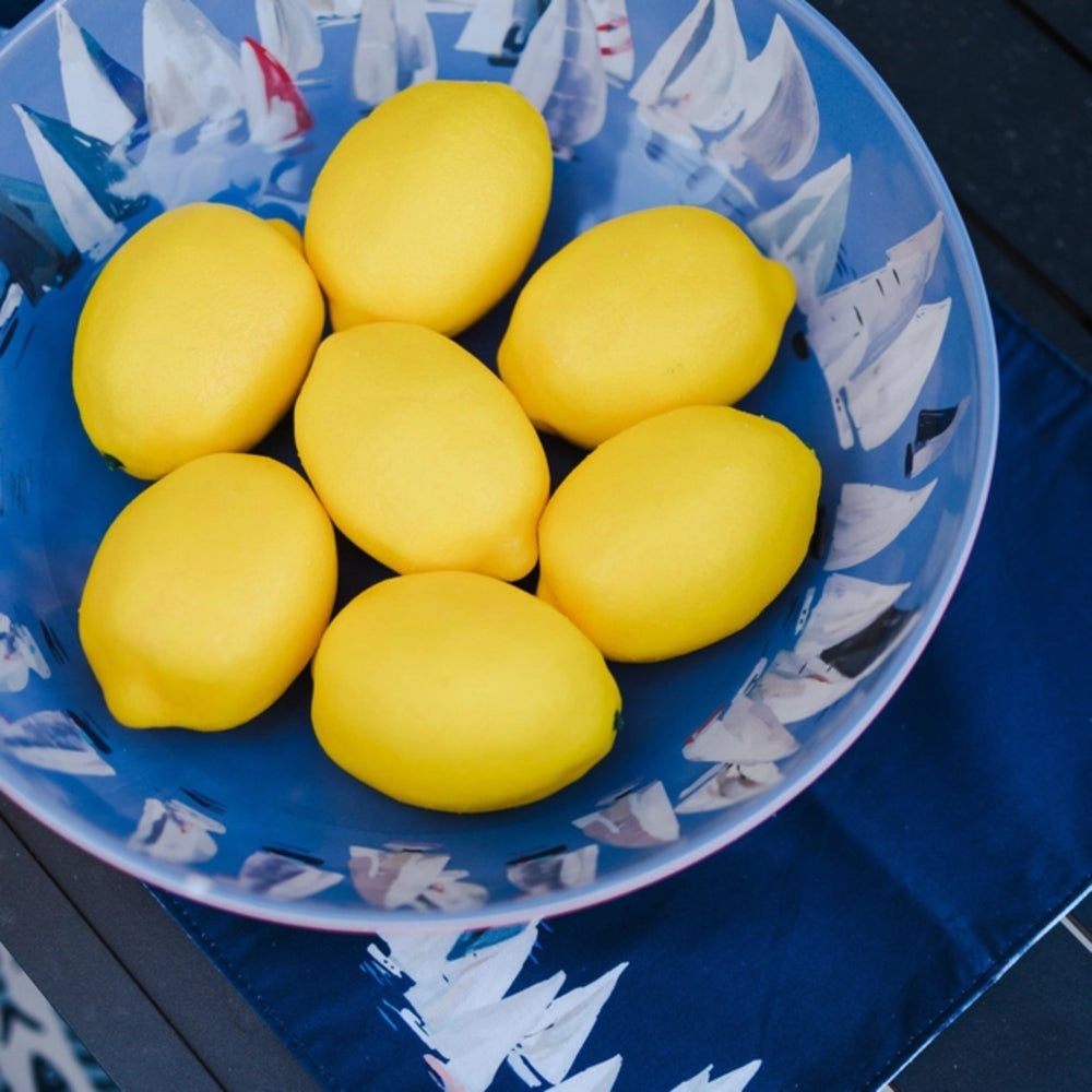 Blue bowl with white sailboat pattern containing yellow lemons on a blue surface.
