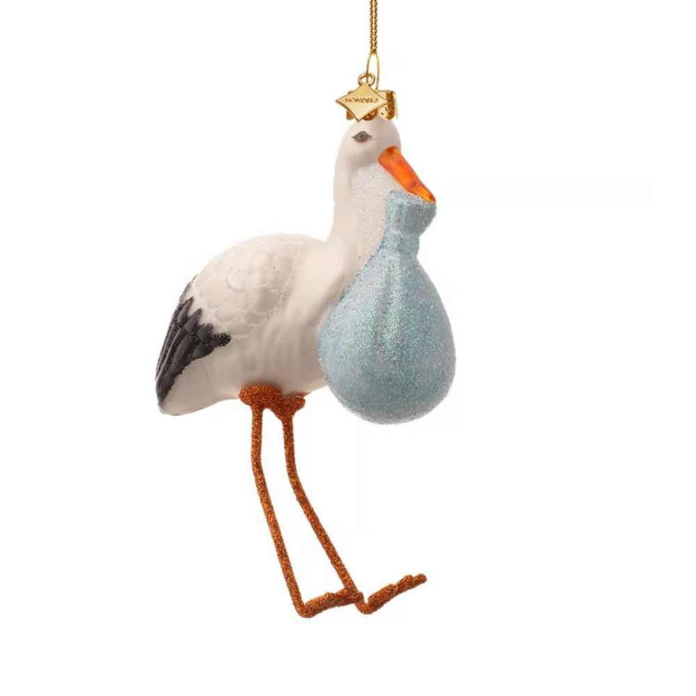 A stork-shaped hanging ornament with a white body, orange beak and legs, black wing accents, and a glittery light blue sack under its wing. A gold hanging loop is attached at the top against a plain white background.
