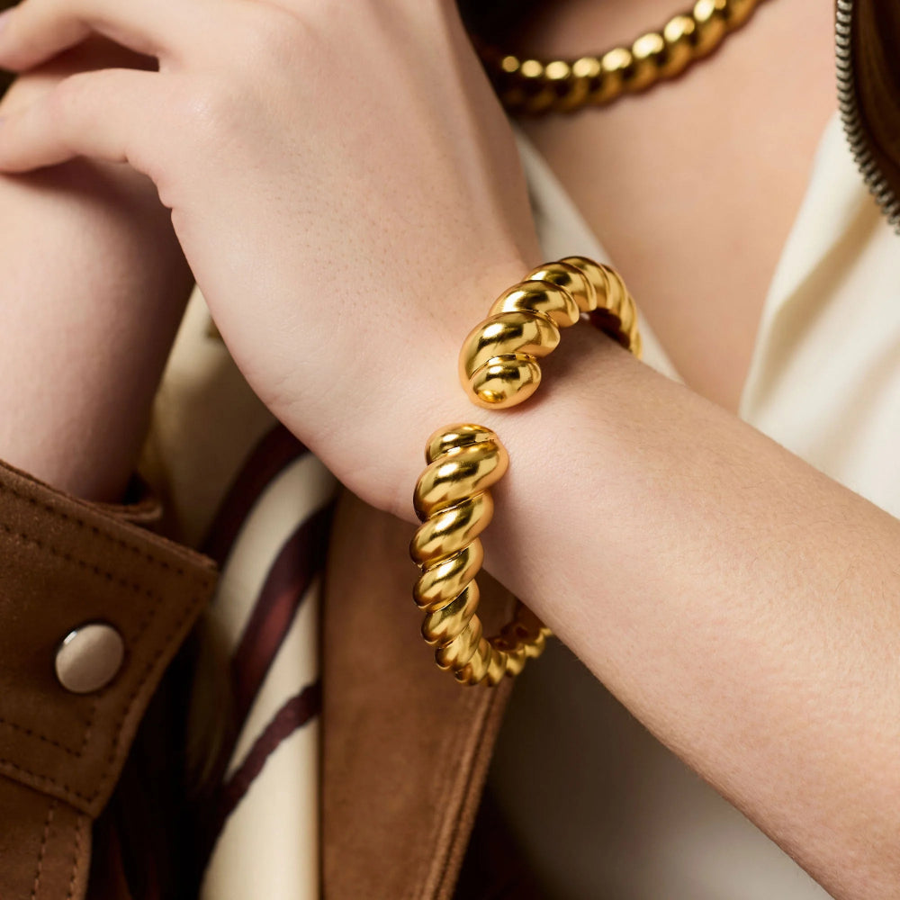 Gold bracelets on a person's wrist with a neutral background