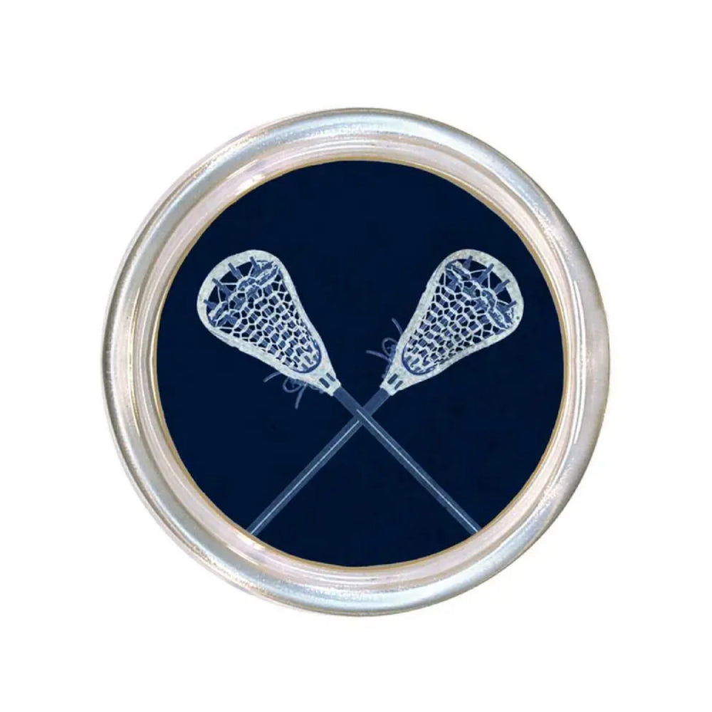 Round glass coaster with a rim and white lacrosse sticks on a navy blue base on a white backround 
