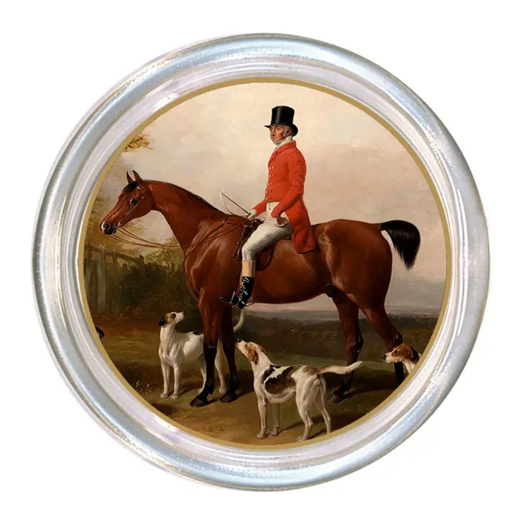 A round decorative coaster featuring a classic equestrian painting of a rider on a brown horse with two dogs, surrounded by a silver-toned metallic border.