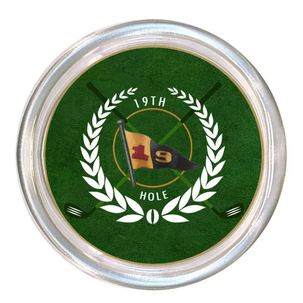A round golf-themed coaster or decorative plaque featuring a green background with a white laurel wreath, crossed golf clubs, a flag with the number 19, and the text '19TH HOLE'. The item has a metallic silver rim and is shown on a plain white background.