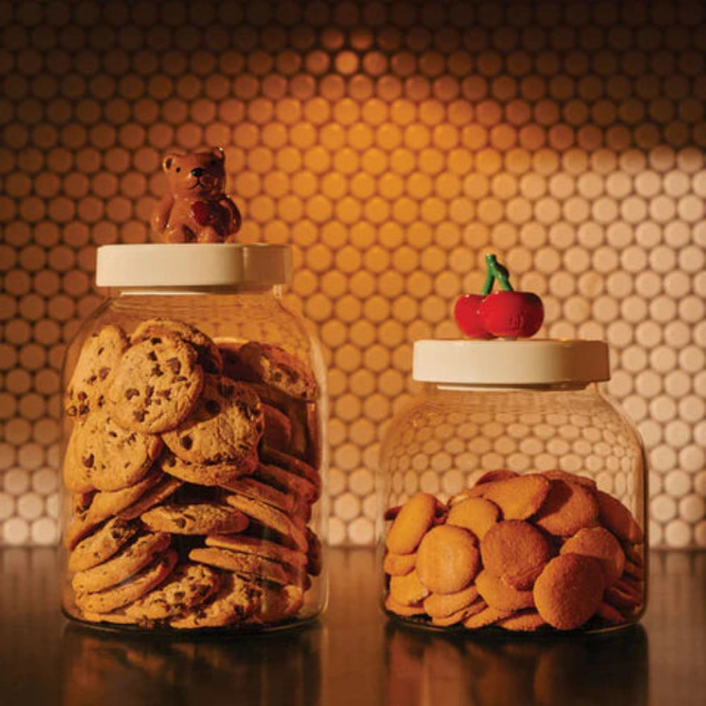Two jars filled with cookies on a reflective surface with a patterned wall in the background.