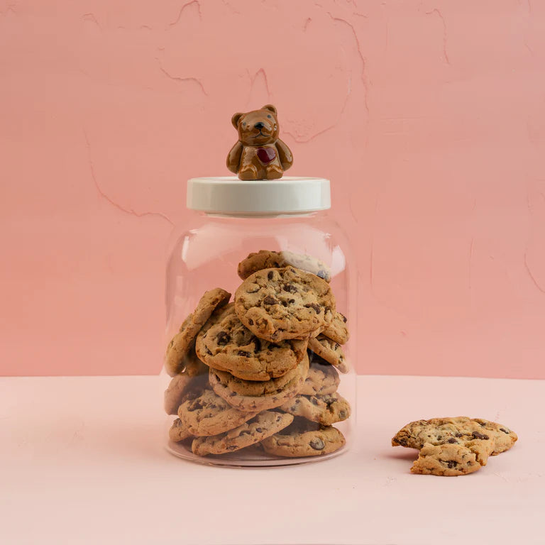 Jar of cookies with a teddy bear on top against a pink background.