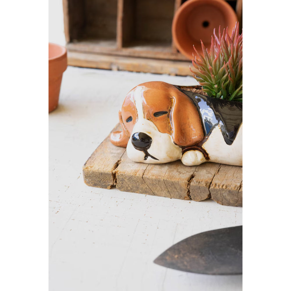 Dog-shaped planter on a wooden surface with plants in the background