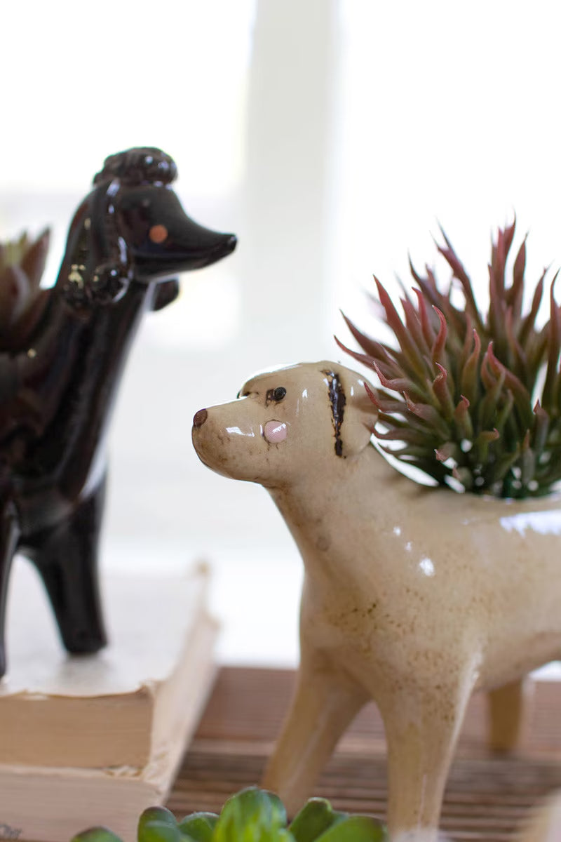 Two ceramic dog figurines with a plant on a wooden surface.