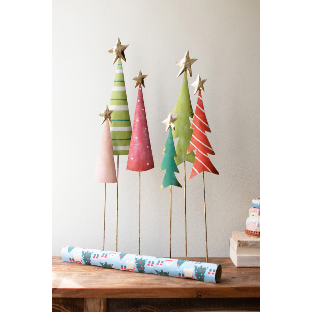 Colorful paper Christmas trees on sticks with a roll of patterned paper on a wooden surface.
