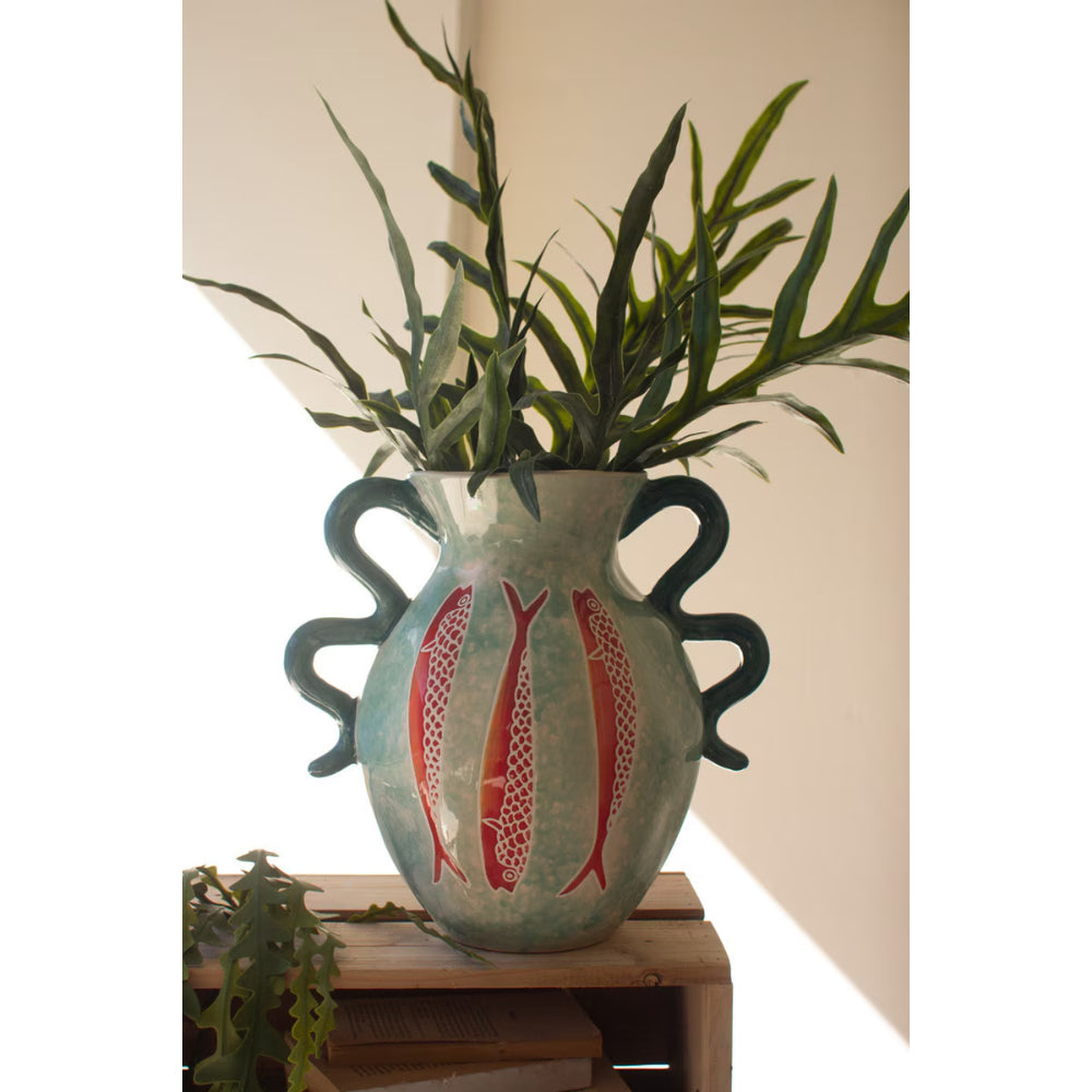 Ceramic vase with fish design and green plant on a wooden surface
