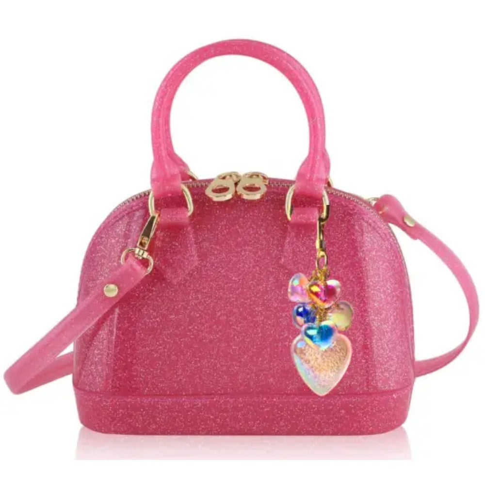 A pink glitter dome handbag with gold-tone hardware, dual top handles, a detachable shoulder strap, and a dangling heart-shaped charm with colorful beads, shown on a white background.