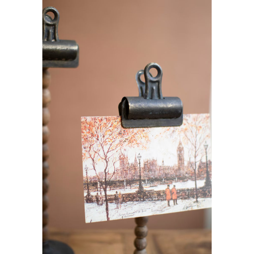 Metal clip holding a postcard with a snowy scene of a cityscape.
