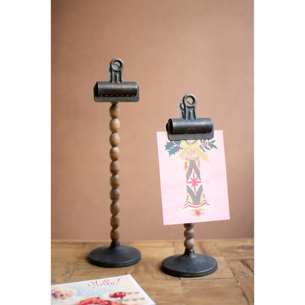 Two wooden clip stands with metal clips on a wooden surface against a brown background