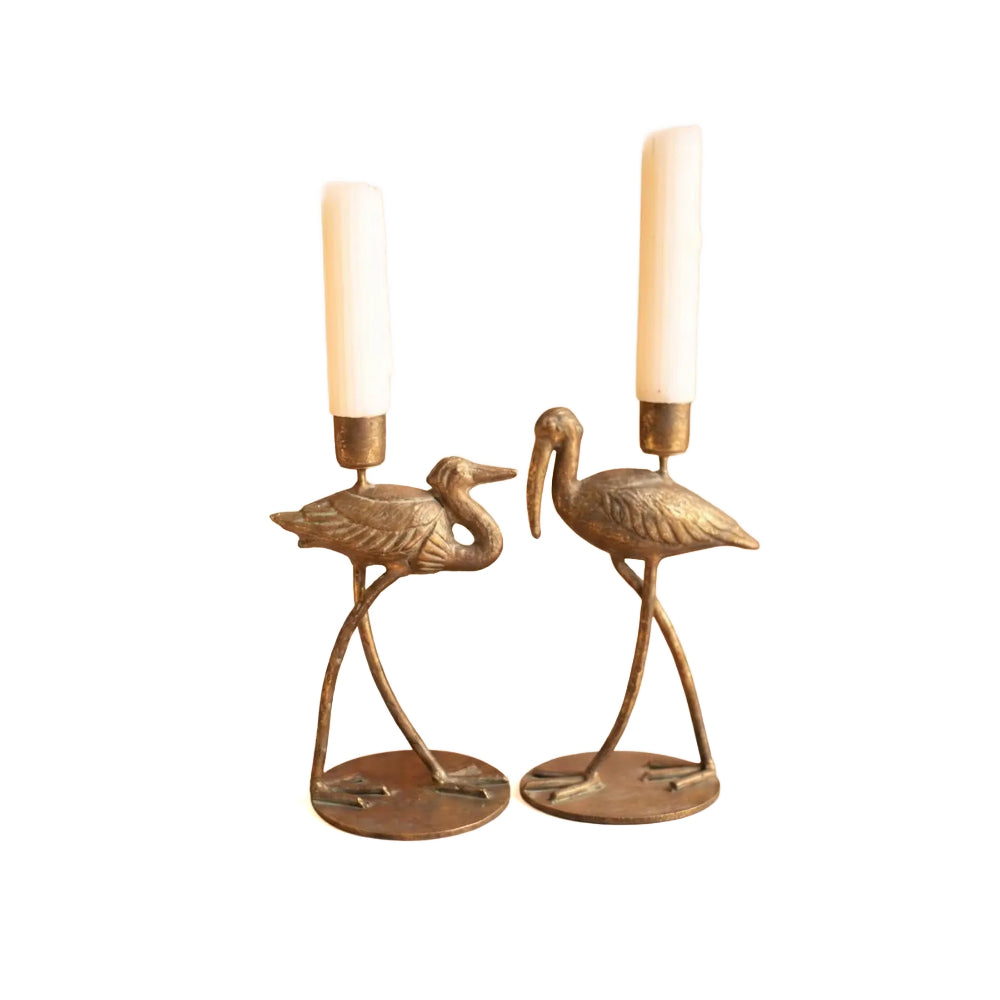 A pair of vintage-style brass or bronze bird candle holders shaped like herons, each holding a white pillar candle, set against a plain white background.