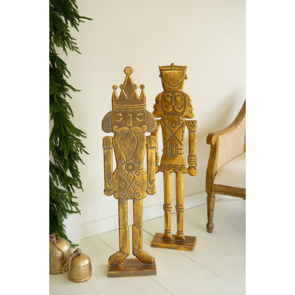 Two gold nutcrackers standing on a white floor with a Christmas tree in the background.