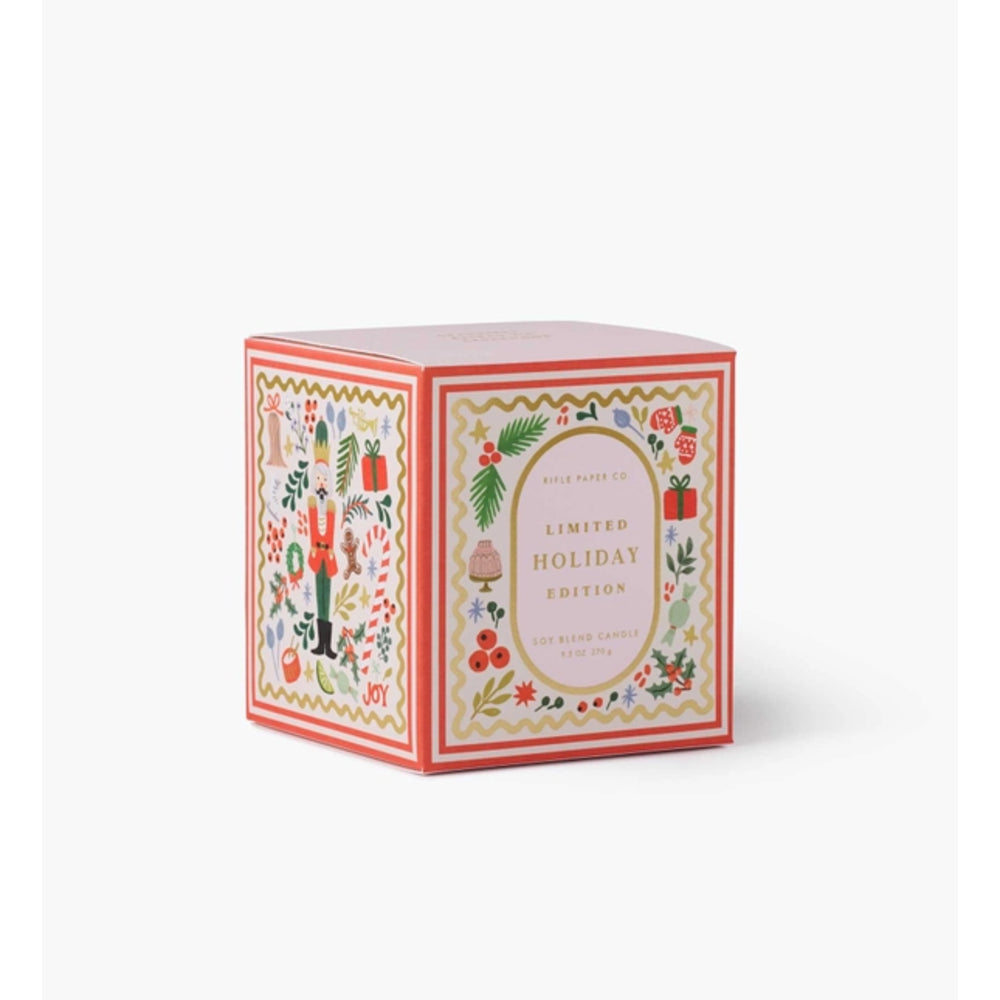 A square decorative product box for a holiday candle, featuring a cream background with red borders and colorful Christmas illustrations including a nutcracker, ornaments, and pinecones. The front label reads 'Wild Bessie Co.