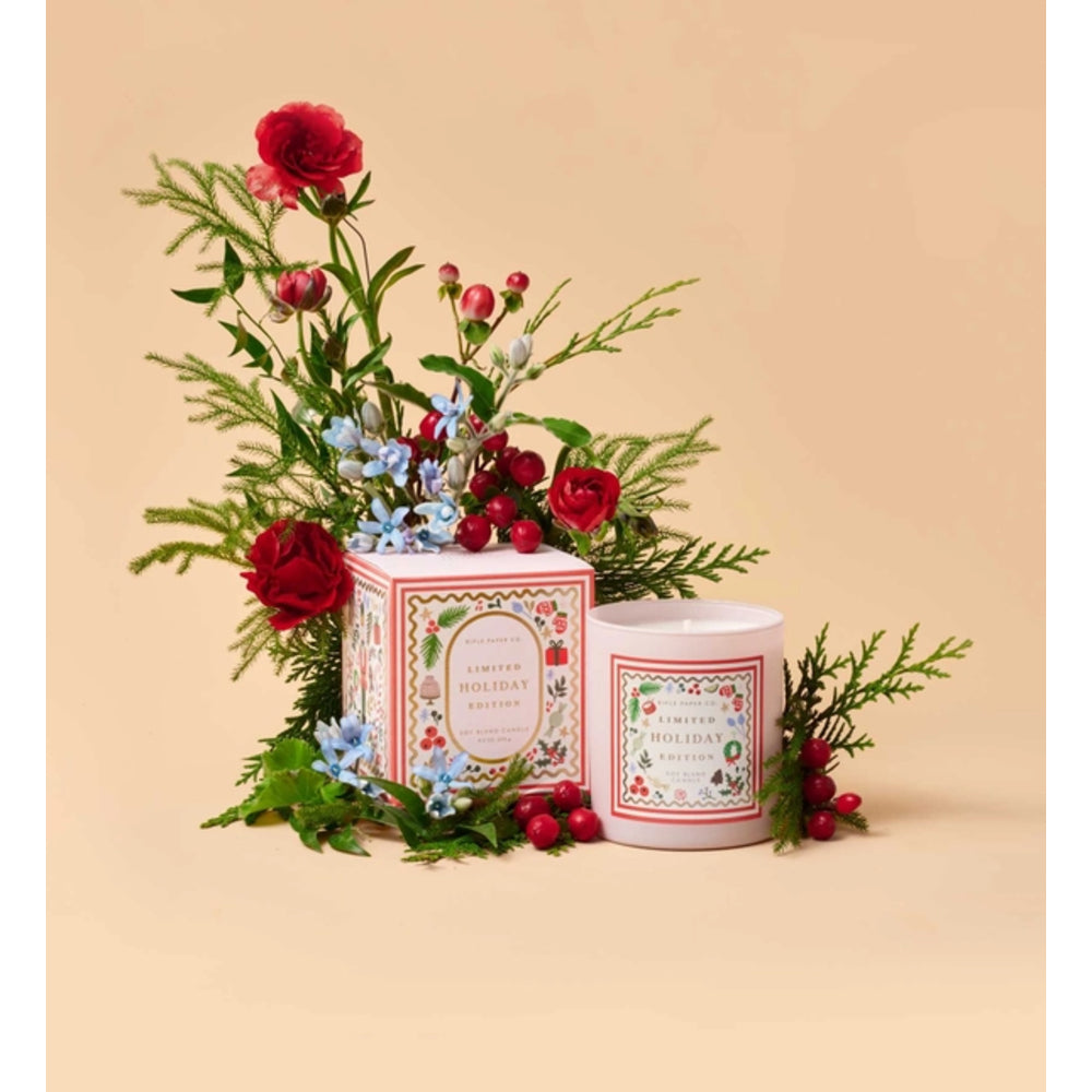 A candle product shown with its decorative box and a matching candle jar, styled with red roses, green foliage, and small blue flowers on a warm beige background. The labels read 'Winter Holiday Scents' and 'Winter Wonderland Candle.