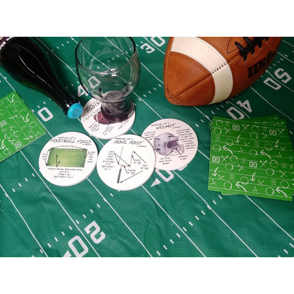 A football-themed party game set laid out on a green football field print background, including a brown and white football, a clear stemware holder, several round printed tokens, and green playcard-style pieces.