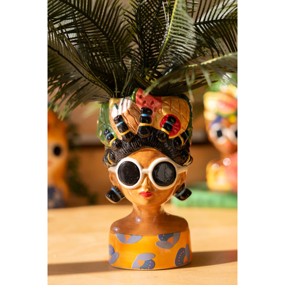Decorative figurine with colorful headpiece and sunglasses on a wooden surface.