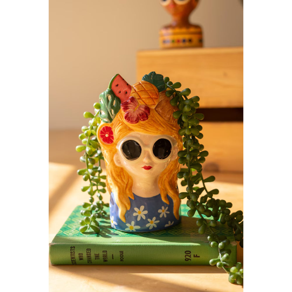 Decorative figurine of a girl with flowers and a watermelon on her head, placed on a book with green leaves.