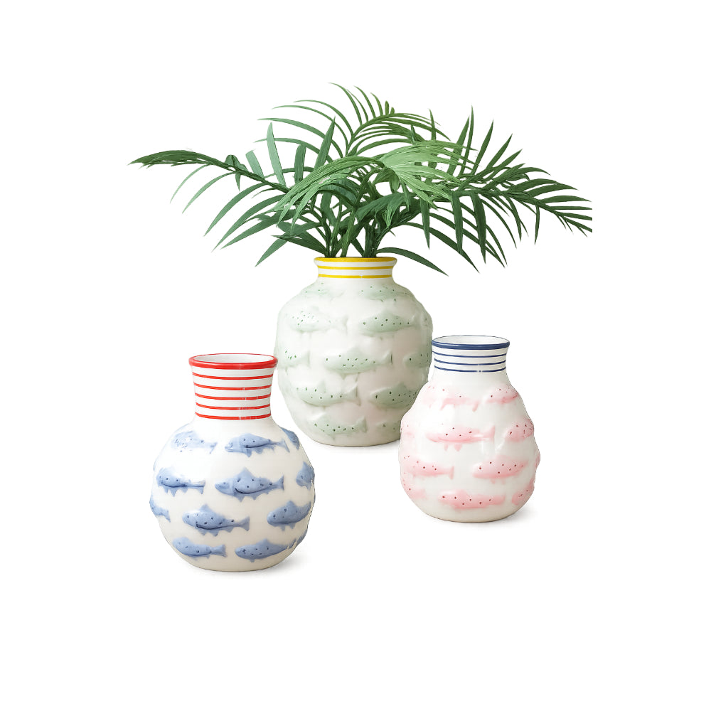 Three decorative ceramic vases with fish patterns in blue, green, pink, red, and navy, with a green palm plant inserted into the tallest vase, on a white background.