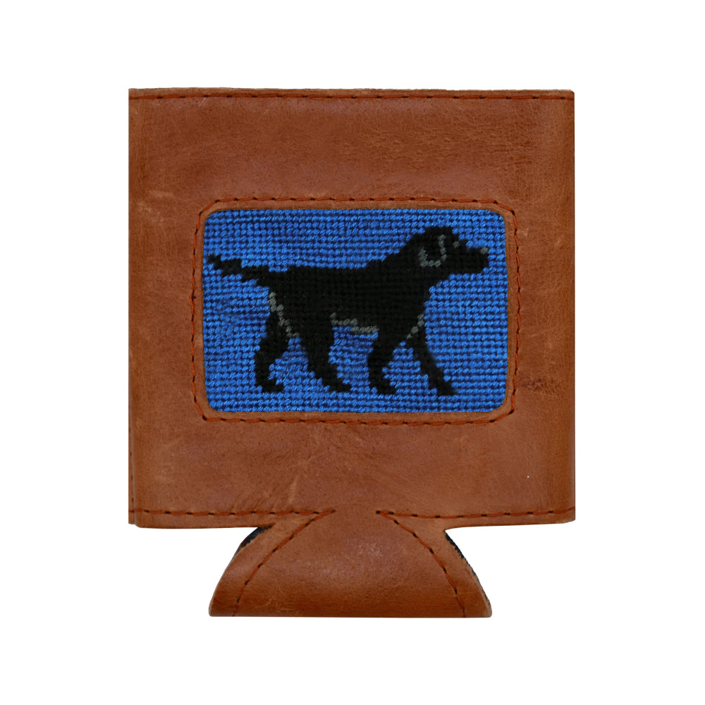 A brown leather can cooler with a needlepoint image of a Black Labrador Retriever against a light blue background  laying flat on a white background. 