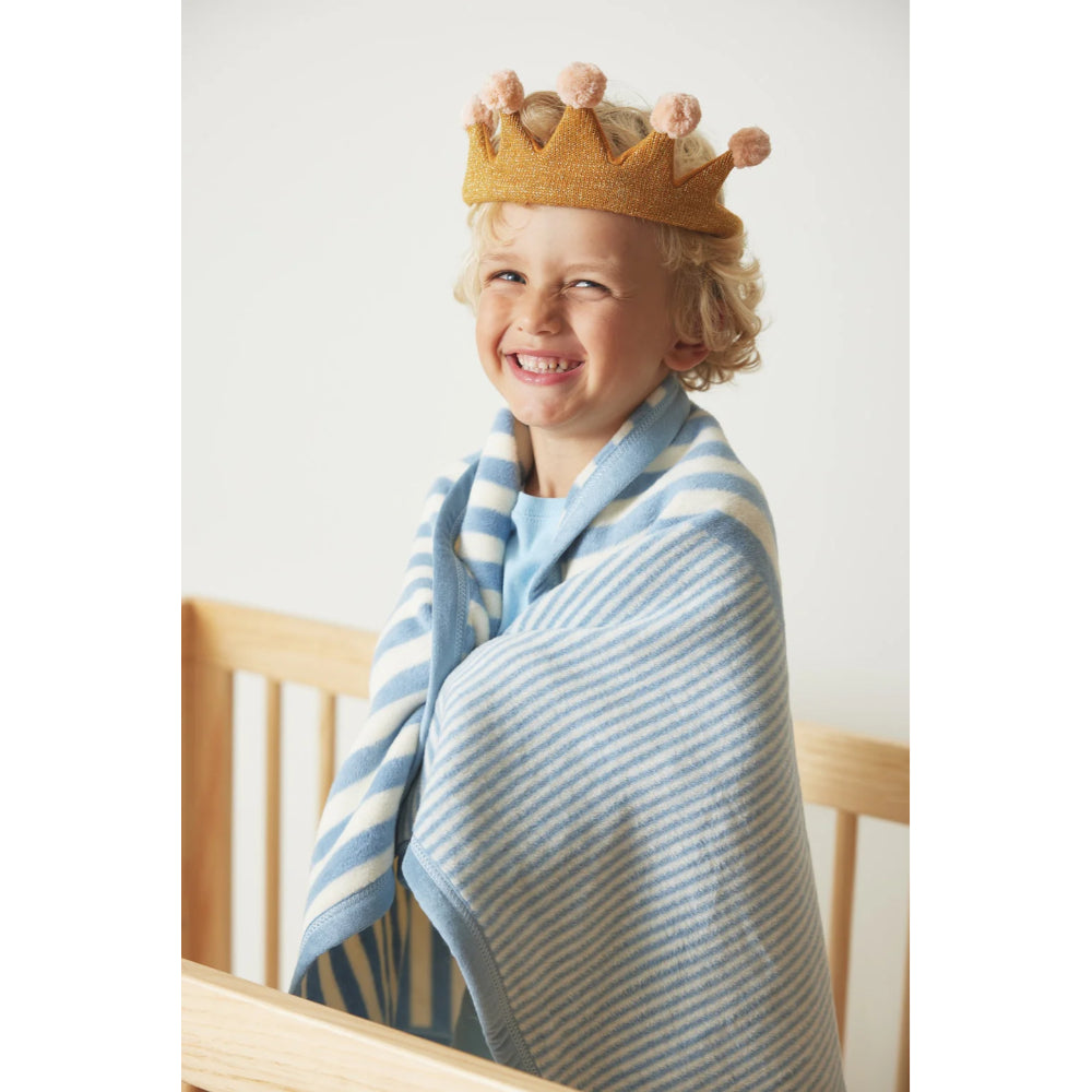 Child wearing a crown and a blue and white striped blanket, sitting on a wooden surface.