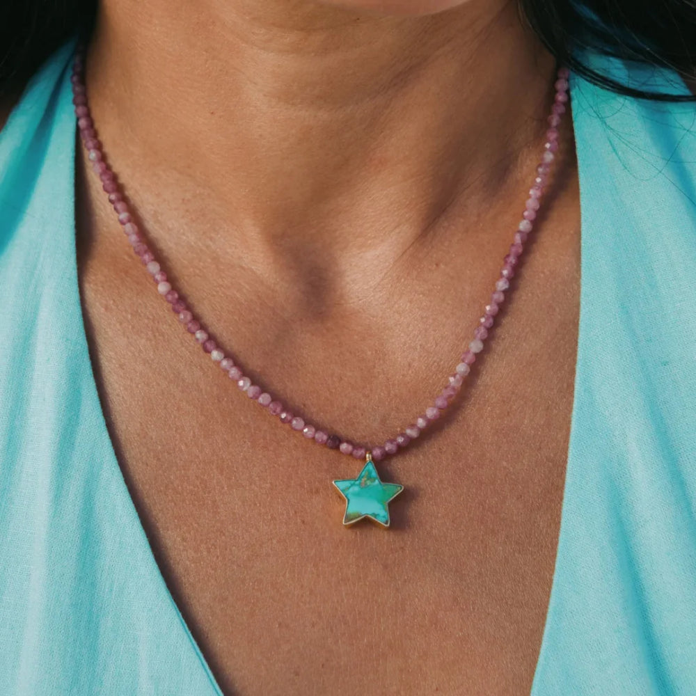 A close-up of a person wearing a beaded necklace with a turquoise star pendant, paired with a light blue top.