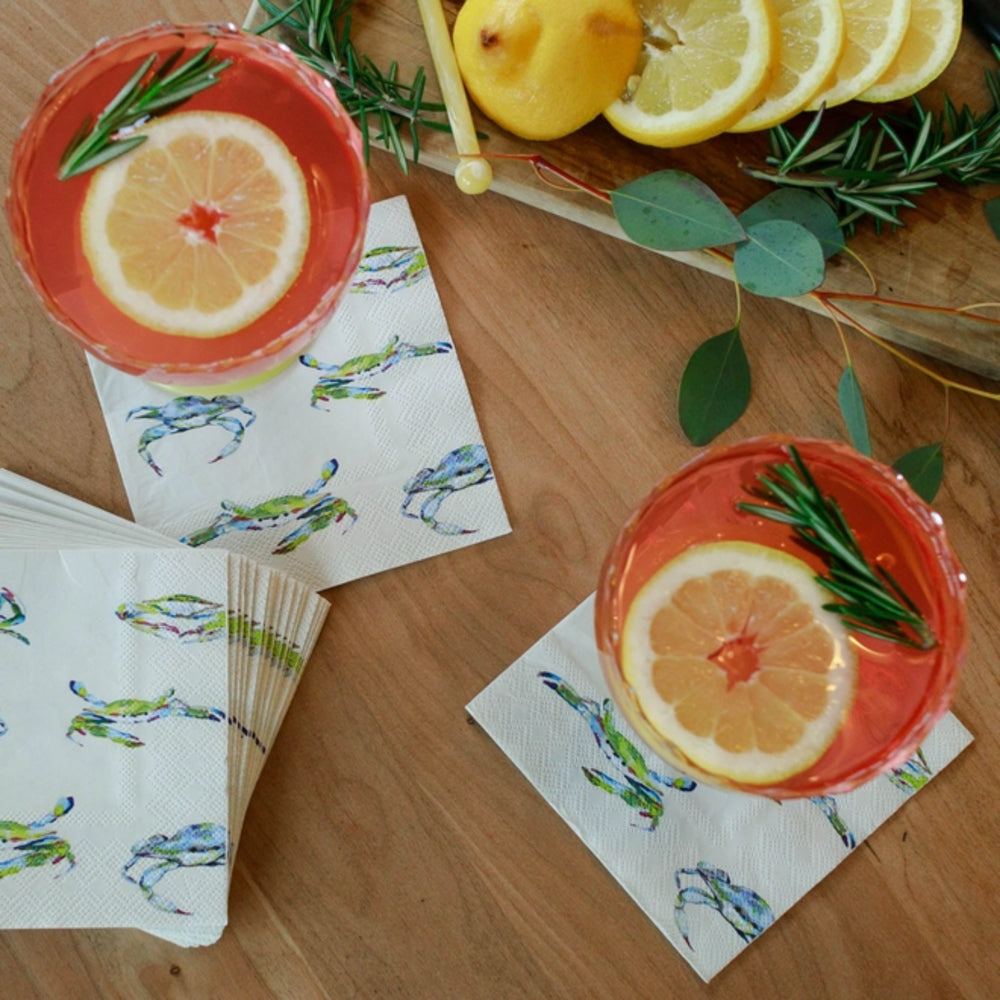 Two glasses of red drinks with lemon slices and rosemary on a wooden table with patterned napkins.