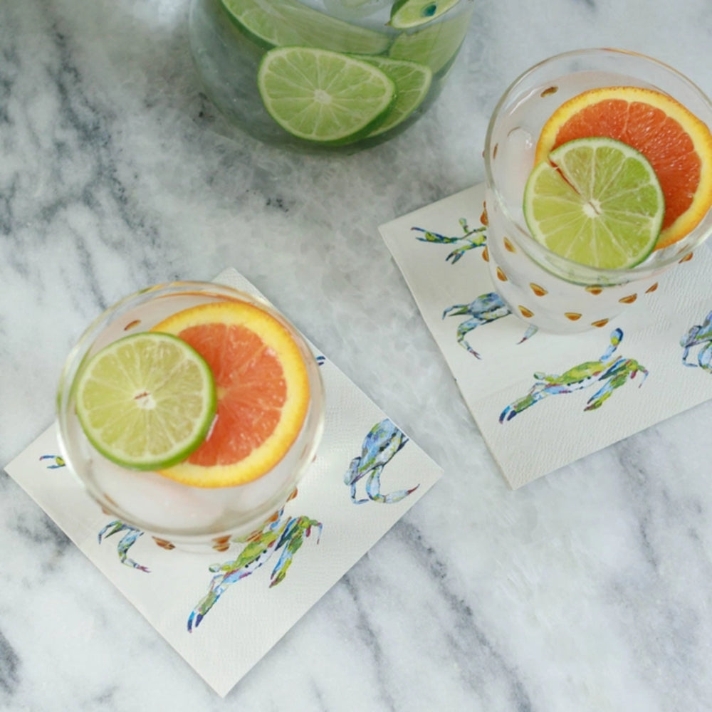 Two glasses of citrus-themed cocktails on decorative napkins with a marble background.