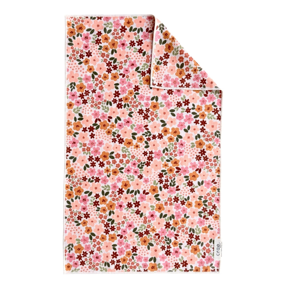 A folded cotton kitchen towel with a dense pink, orange, and green floral pattern, shown on a clean white background.