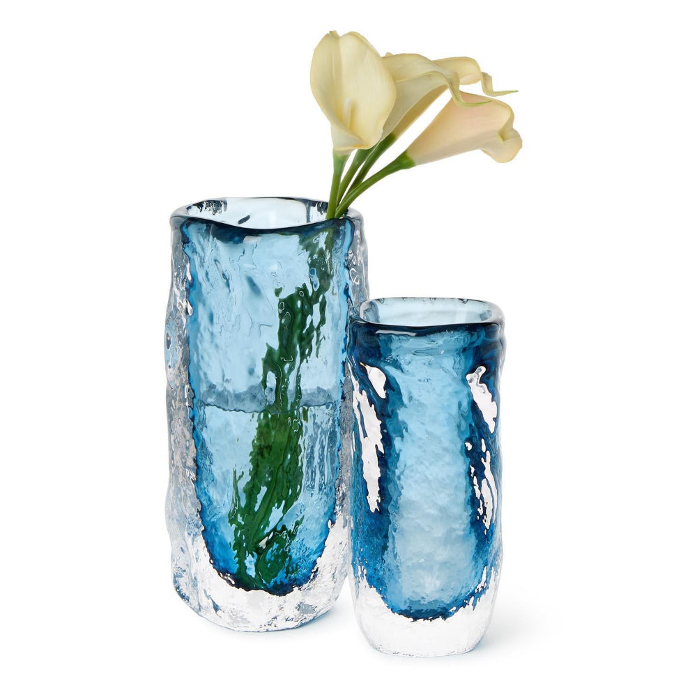 Two textured glass vases in shades of blue and white, with pale yellow flowers in the taller vase, set against a plain white background.