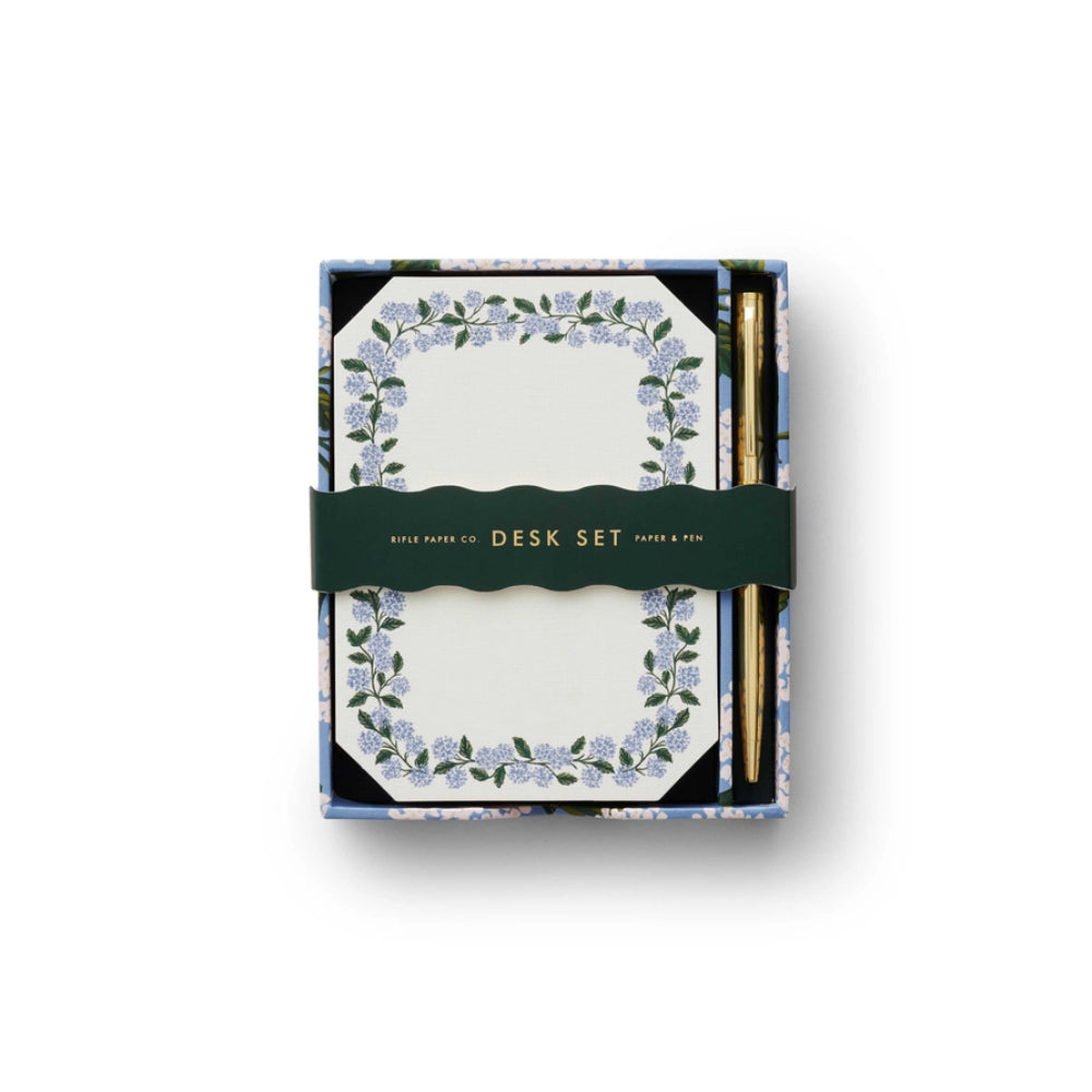 A note writing set by Rifle Paper Co. featuring hydrangea illustrations, including 130 flat notes and a gold pen, packaged in a desktop box.