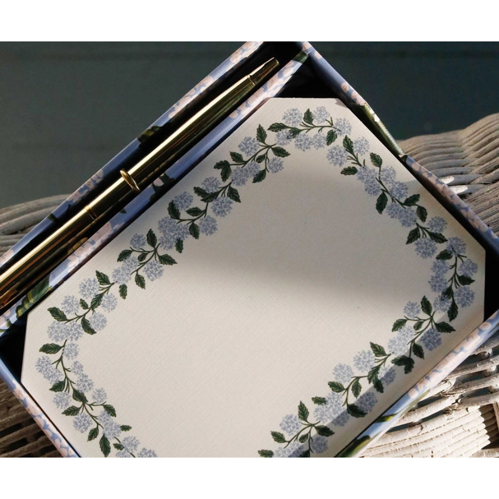 Decorative paper with floral border and pen on wooden surface on a green backround.
