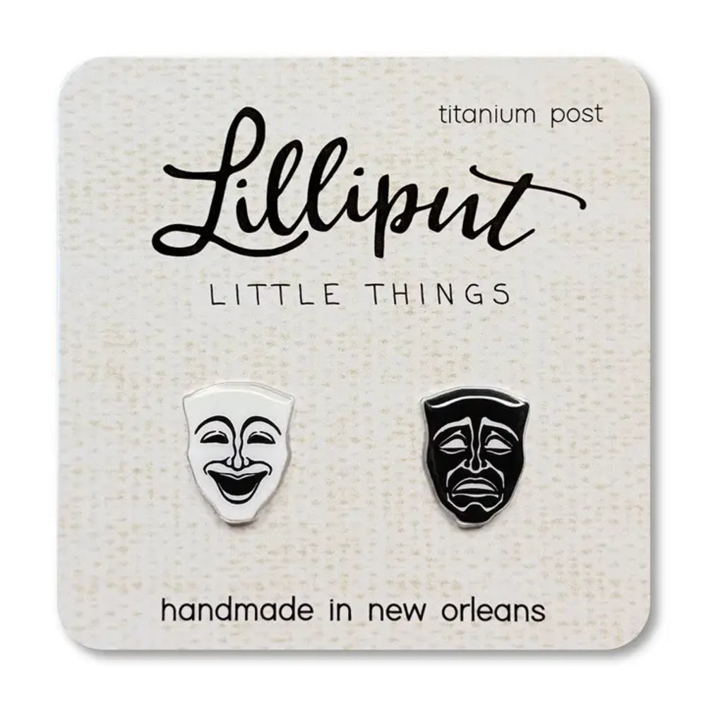 A pair of titanium post stud earrings shaped like comedy and tragedy theater masks, displayed on a textured cream card labeled 'Lilliput LITTLE THINGS'.